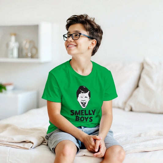 Child wearing a green t-shirt with 'SMELLY BOYS' text and graphic, sitting on a bed.