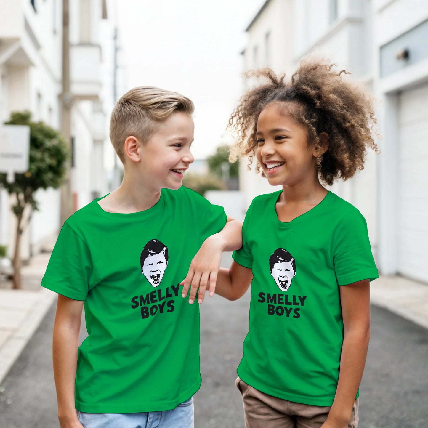 Two children wearing green t-shirts with 'Smelly Boys' text and graphic, standing on a street.