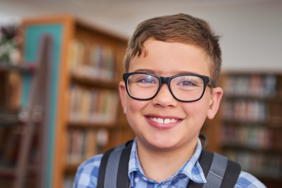 Young boy with glasses smiling in a library setting