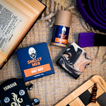 A carton of soap and tube of deodorant arranged on a beige blanket next to a book and chess board
