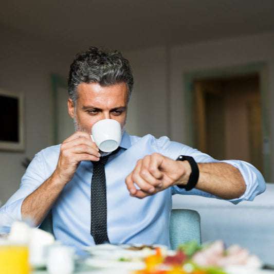 Man dressed for office is having early breakfast and checking his watch