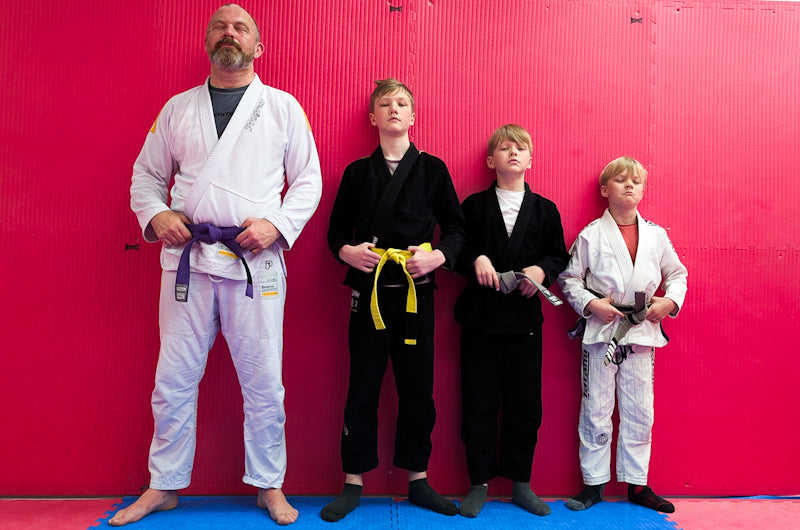 Four individuals in martial arts uniforms standing against a red wall.