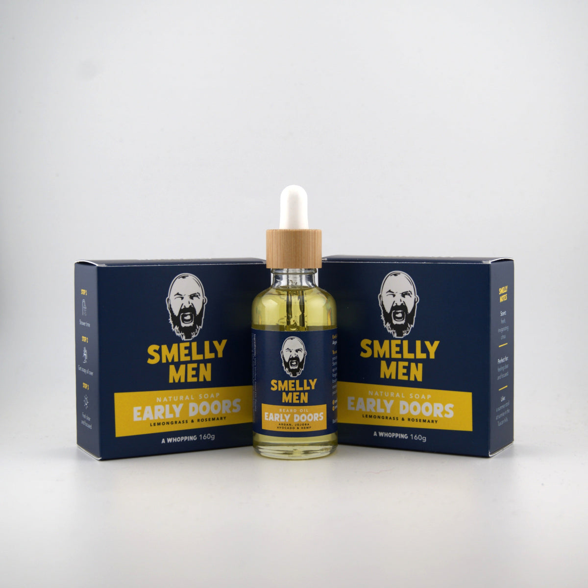 A bottle of Smelly Men Natural Early Doors beard oil with a dropper cap, flanked by two navy blue and yellow natural soap cartons on a light grey background.