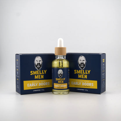 A bottle of Smelly Men Natural Early Doors beard oil with a dropper cap, flanked by two navy blue and yellow natural soap cartons on a light grey background.