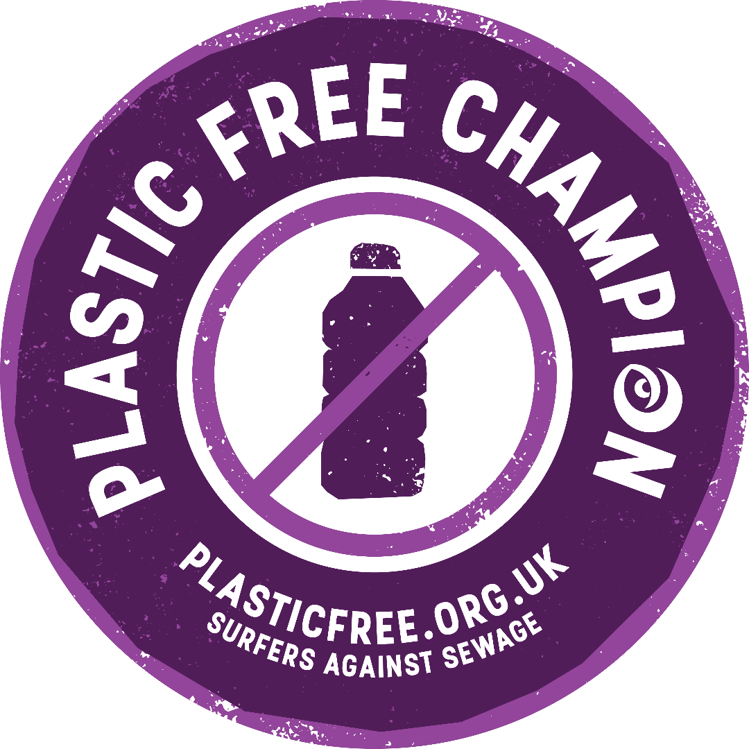 A circular purple sticker or badge with distressed edges reading 'PLASTIC FREE CHAMPION' around the perimeter, a plastic bottle icon crossed out in the center, and 'PLASTICFREE.ORG.