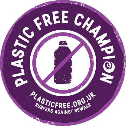 A circular purple sticker or badge with distressed edges reading 'PLASTIC FREE CHAMPION' around the perimeter, a plastic bottle icon crossed out in the center, and 'PLASTICFREE.ORG.