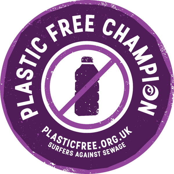 A circular purple sticker or badge with distressed edges reading 'PLASTIC FREE CHAMPION' around the perimeter, a plastic bottle icon crossed out in the center, and 'PLASTICFREE.ORG.