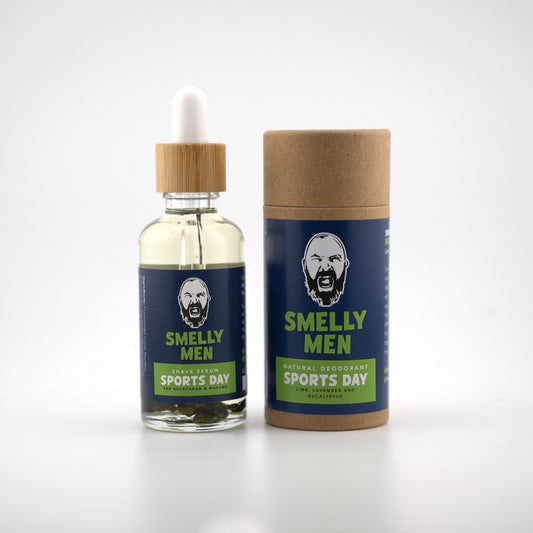 A bottle of sports day deodorant oil with a wooden dropper cap stands next to its brown cardboard tube packaging. Both containers feature a dark blue label with a cartoon bearded man's face and the text 'SMELLY MEN' and 'SPORTS DAY'.
