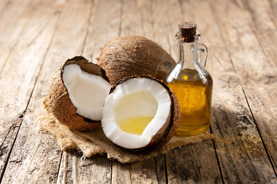 Coconuts and oil in a glass bottle on a wooden table.