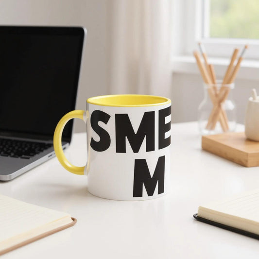 Mug with 'SMELLY MEN' on a desk with a laptop and office supplies.