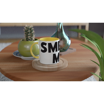 White mug with black text on a wooden table with a plant and decorative items.
