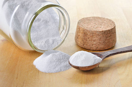 A jar on its side containing sodium hydroxide powder with a cork stopper and a wooden spoon